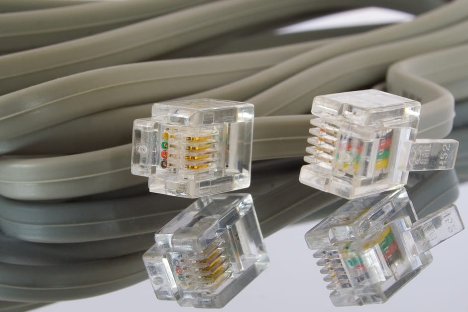 A close-up of several clear plastic Ethernet cables with gold-plated contacts, stacked and intertwined on a reflective surface. The cables are uniformly grey and have a smooth, flexible texture. The c